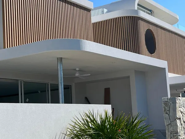 Curved white facade with woodgrain aluminium battens to the balcony and porthole window