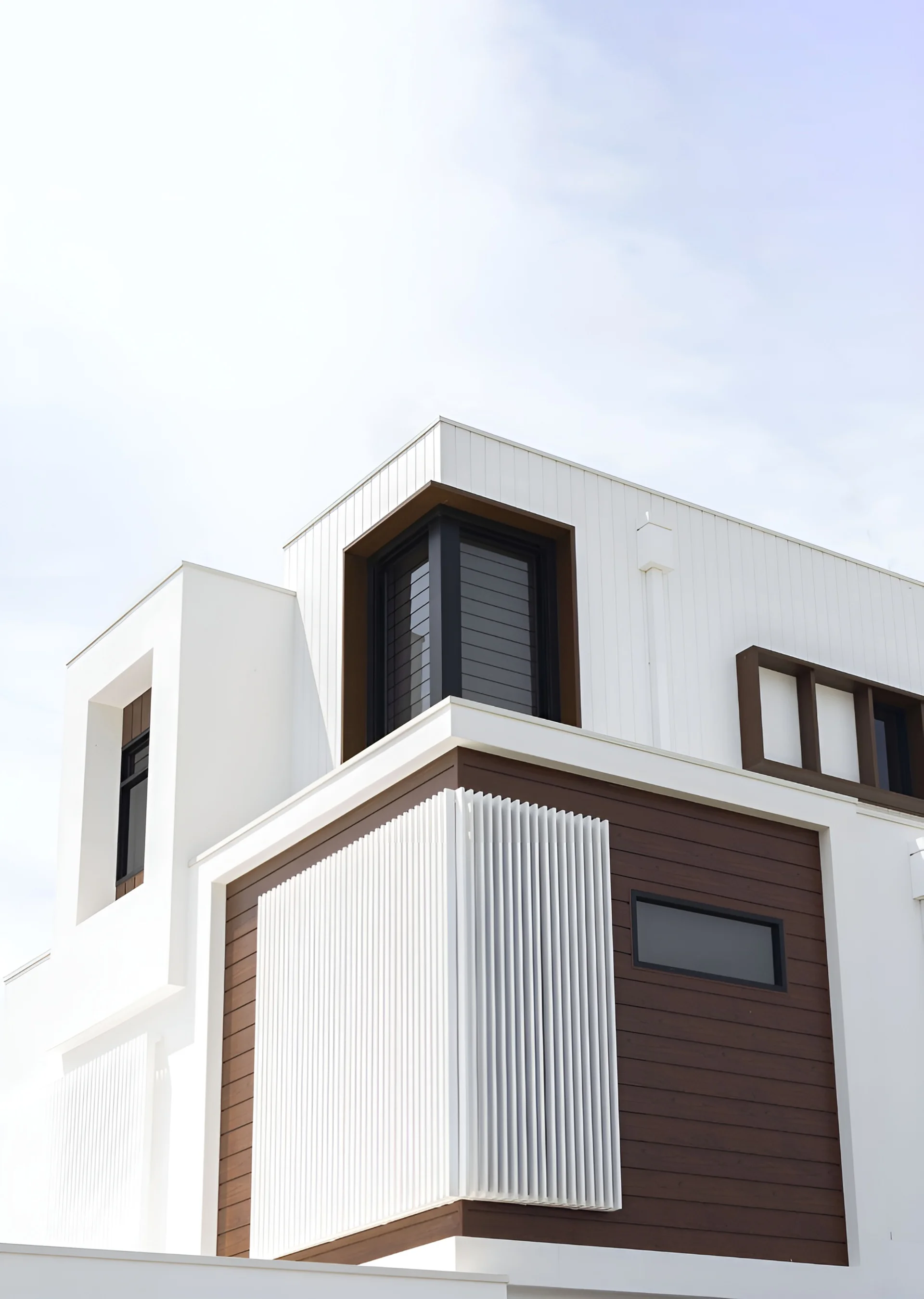 White house facade with dark woodgrain aluminium panels and white vertical battens