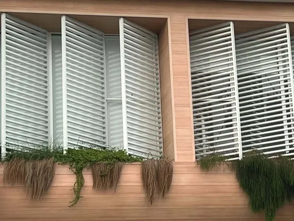 Operable white louvres above a woodgrain aluminium clad balcony wall with trailing plants