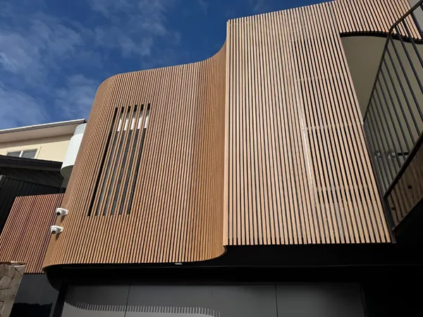 Curved facade corner wrapped in vertical woodgrain aluminium battens