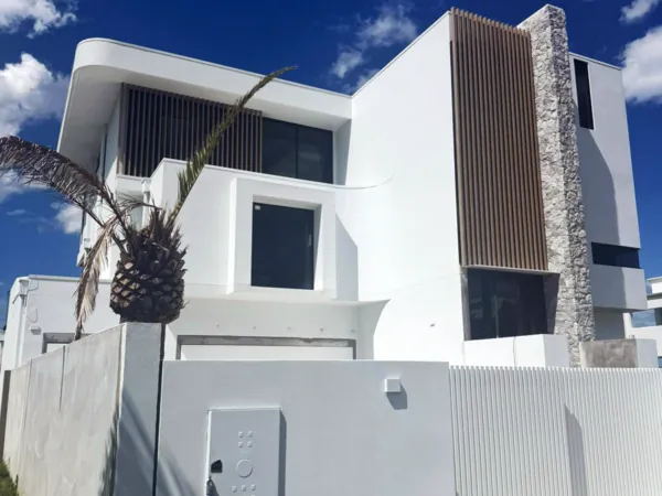 White two-storey home with a woodgrain aluminium batten and stone feature behind a palm