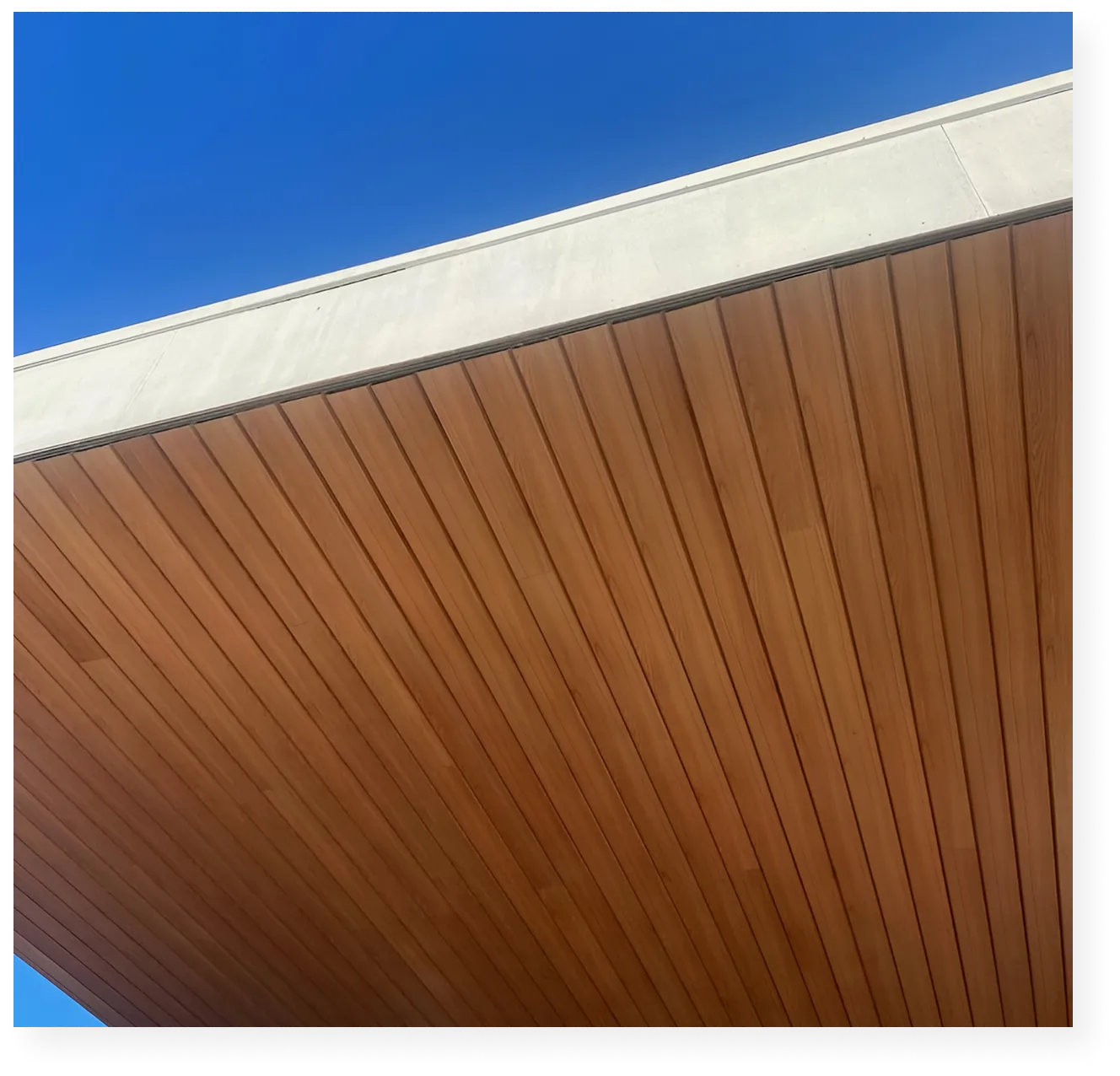 Woodgrain aluminium soffit plane meeting a concrete edge under a clear sky