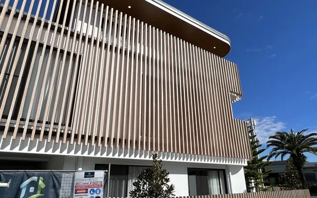 Two-storey corner building wrapped in vertical woodgrain aluminium battens