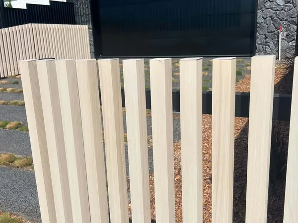 Pale woodgrain aluminium batten fence in front of a dark stone garage wall