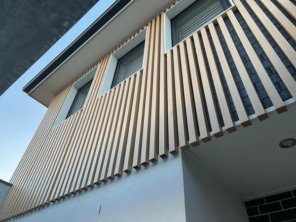 Pale woodgrain aluminium battens wrapping an upper storey above a dark brick base