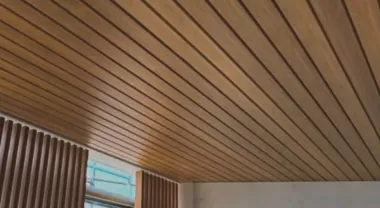Woodgrain aluminium ceiling lining meeting a white wall in an undercover area