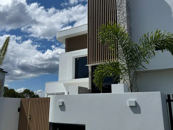 White contemporary home with a dark woodgrain aluminium batten blade feature beside a stone pillar